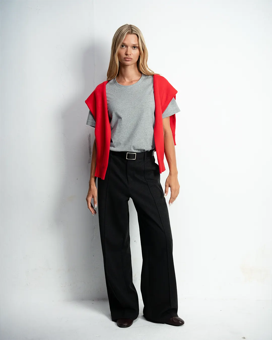 Model in a grey tee and black trousers with a red knit over her shoulders