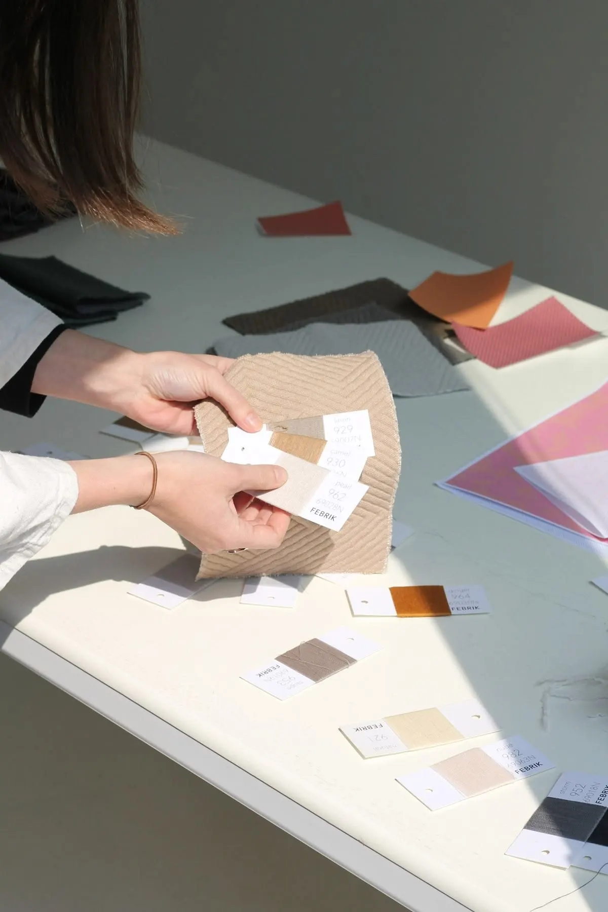 Hands comparing fabric swatches and trim tags
