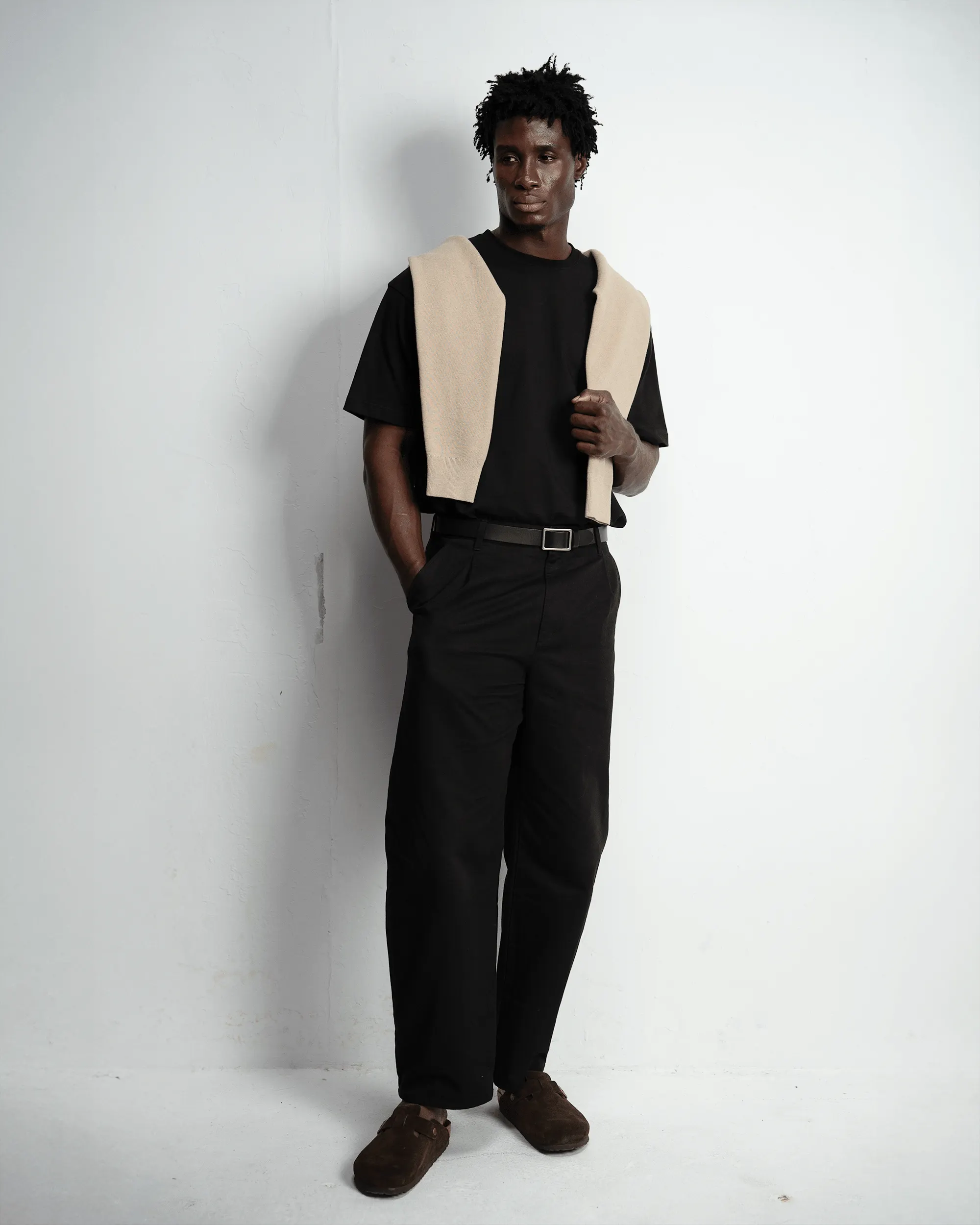 Male model in a black tee and trousers with a knit draped over his shoulders